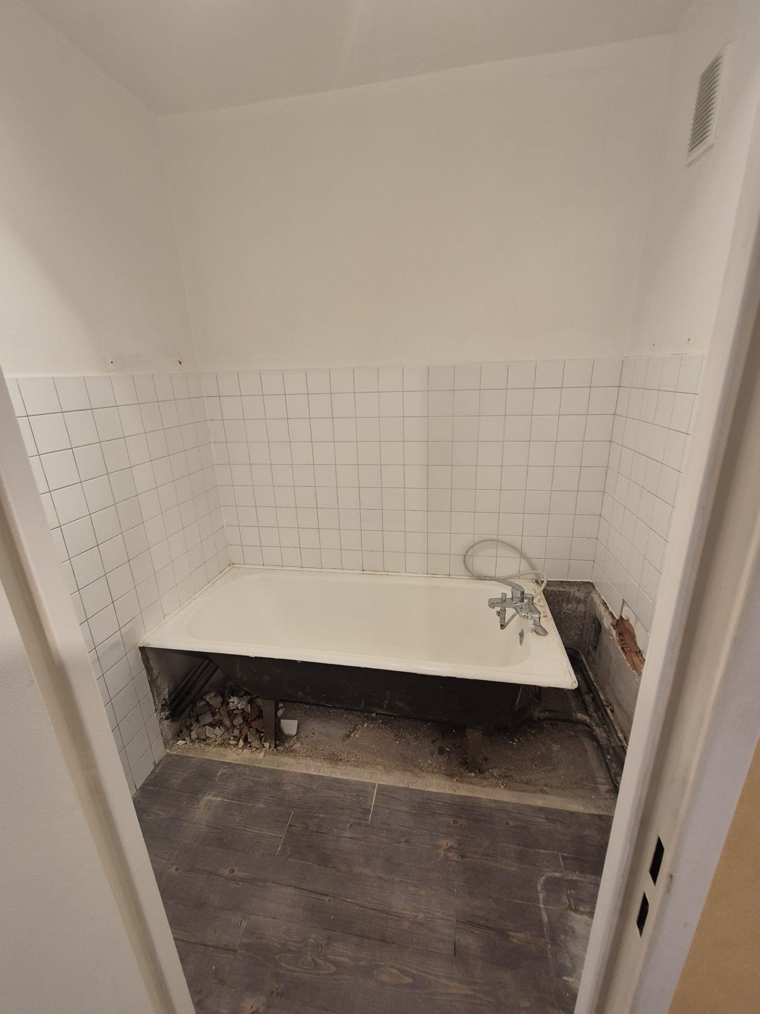 Salle de bain avant travaux : baignoire et faïence blanche abîmée