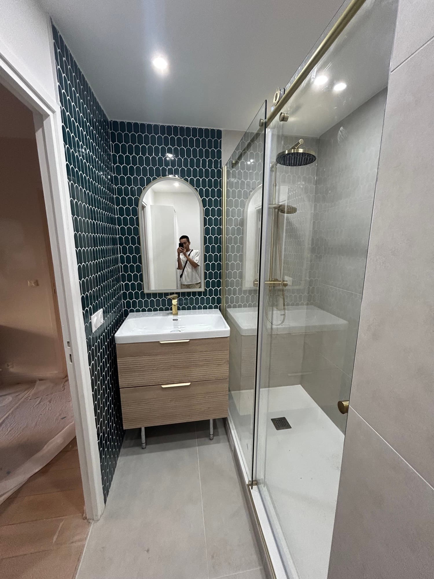 Paris 15e : salle de bain avec faïence en écailles vert sombre, miroir arrondi, meuble vasque bois et douche vitrée